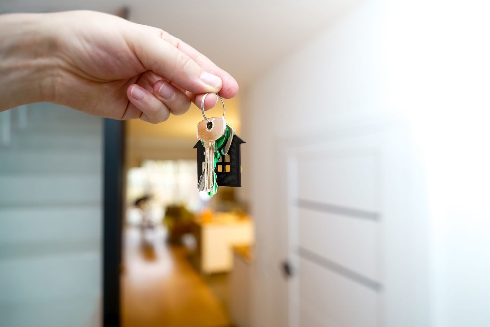 Mão segurando chaves com chaveiro em forma de casa no corredor de uma residência