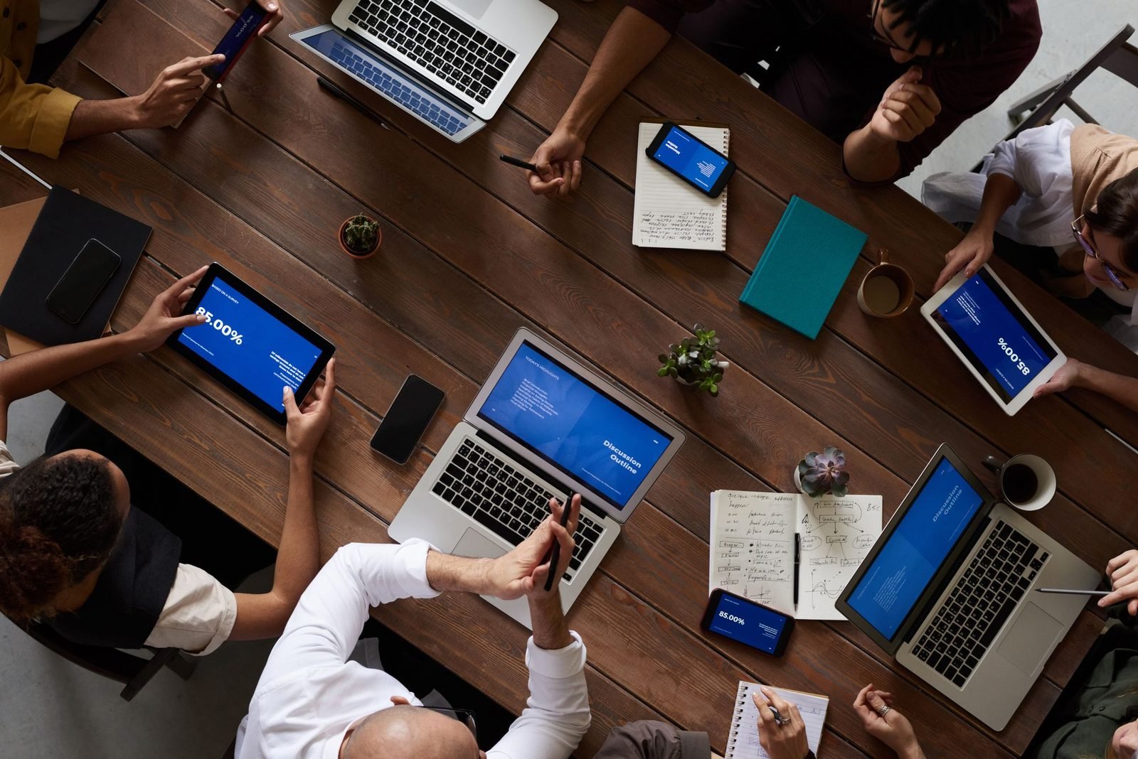 Equipe reunida em volta de uma mesa de madeira, com notebooks, vista de cima