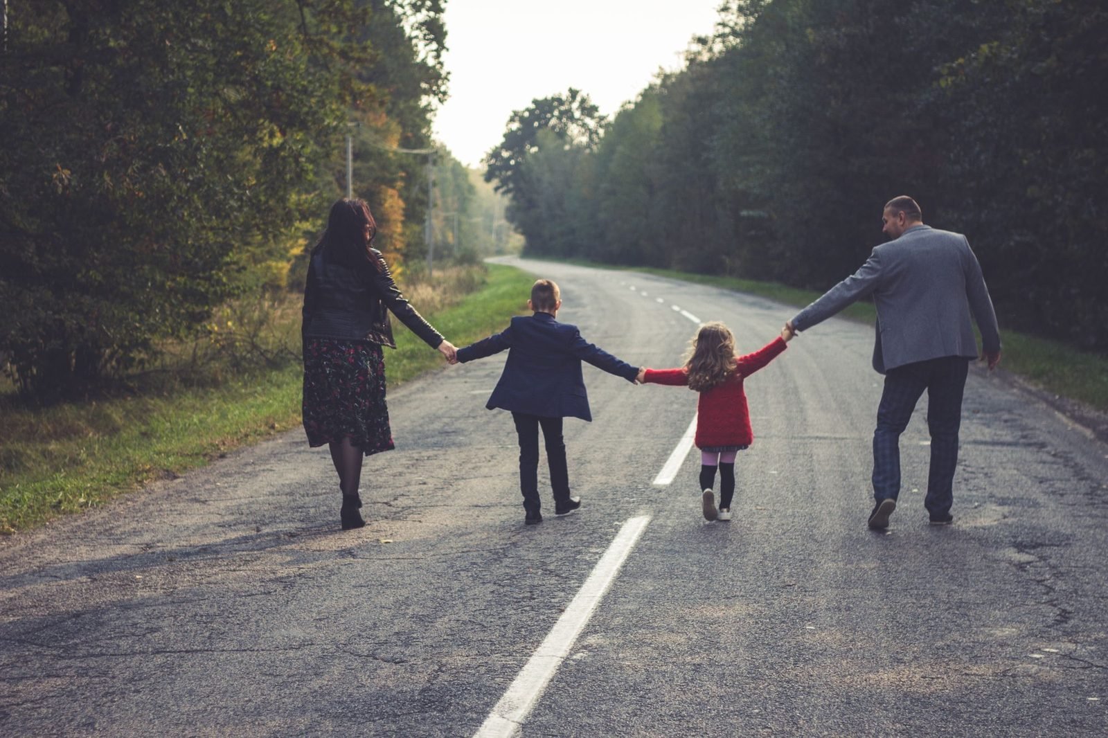 Família caminhando de mãos dadas por uma estrada, vista de costas